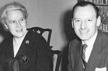 Black-and-white portrait of a smiling woman and man seated together, with bookshelves behind them.