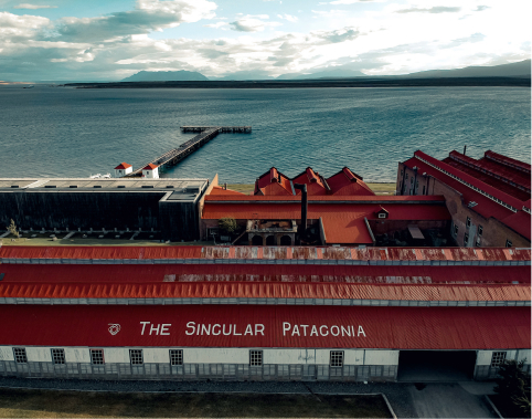 Aerial view of The Singular Patagonia hotel with red roofs, a waterfront pier, and mountains across the bay.