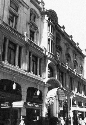 Black-and-white street view of an ornate historic building with arched windows, a grand entrance, and storefronts below.