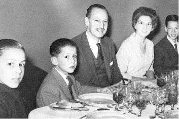 Black-and-white photo of a family seated around a dining table, with a man and woman beside three children