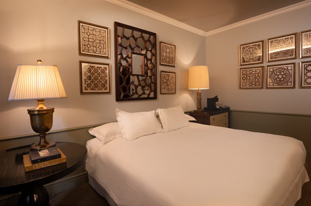 Elegant hotel bedroom with a white bed, warm table lamps, dark wood furniture, and geometric framed wall art.