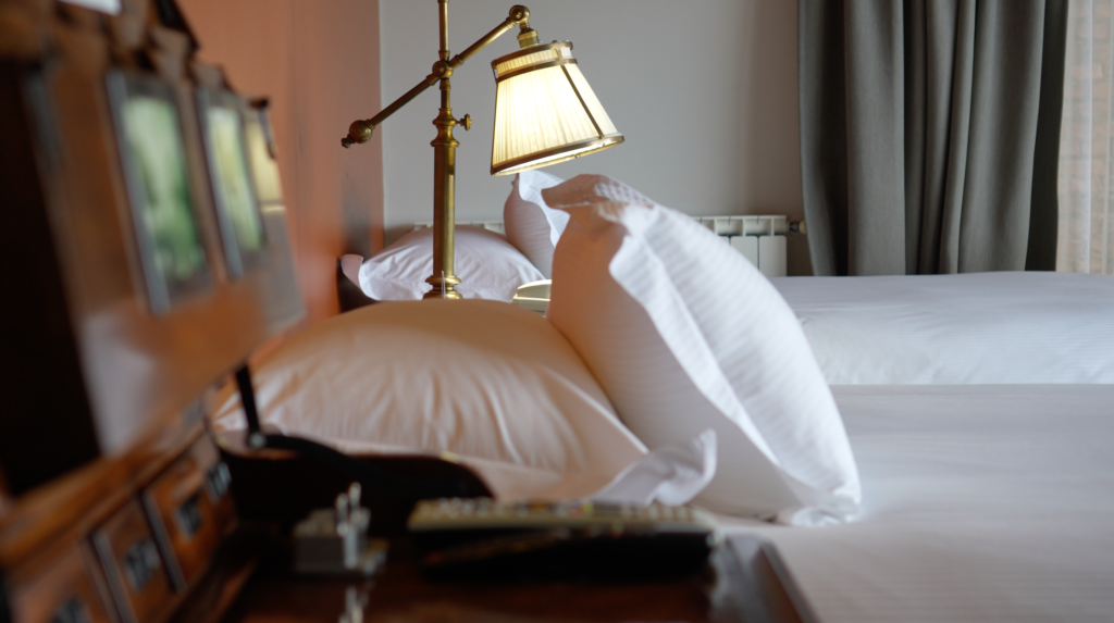 A brass bedside lamp illuminates crisp white pillows and linens in a neatly made bedroom.