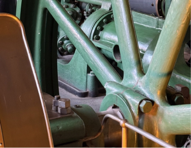 Close-up of green industrial machinery with bolted joints, support beams, and a metal lever beside a brown panel.