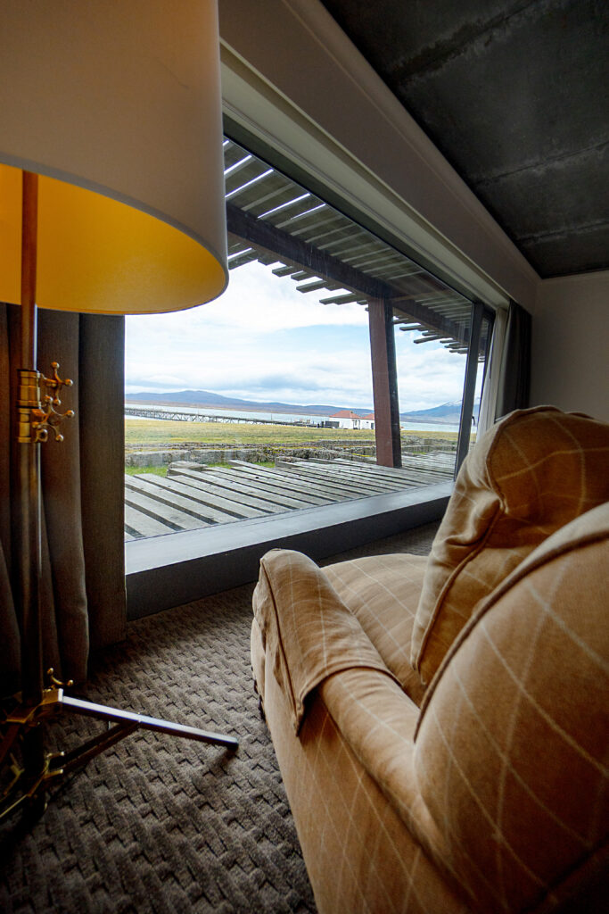 Cozy living room with a sofa and floor lamp overlooking a coastal landscape through a floor-to-ceiling window.
