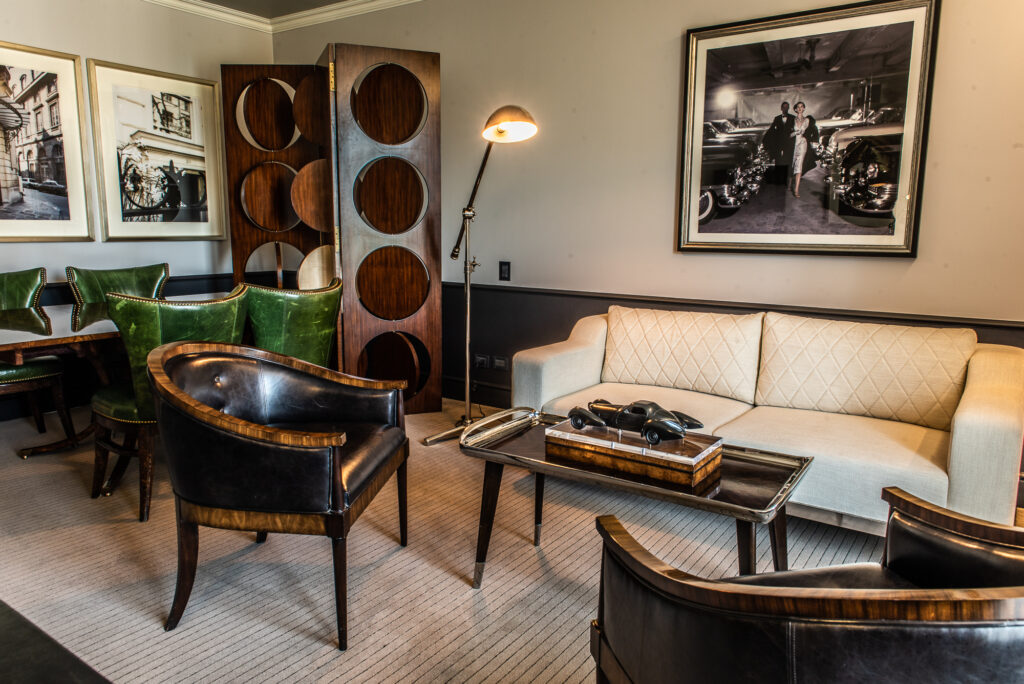 Elegant midcentury modern lounge with a cream sofa, leather chairs, green dining chairs, and a model car on the coffee table.