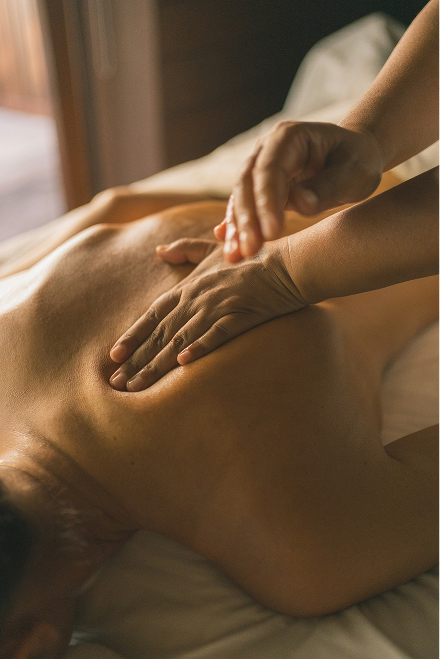 wellness-7 Massage therapist gently massages a client’s back in a warmly lit spa room.