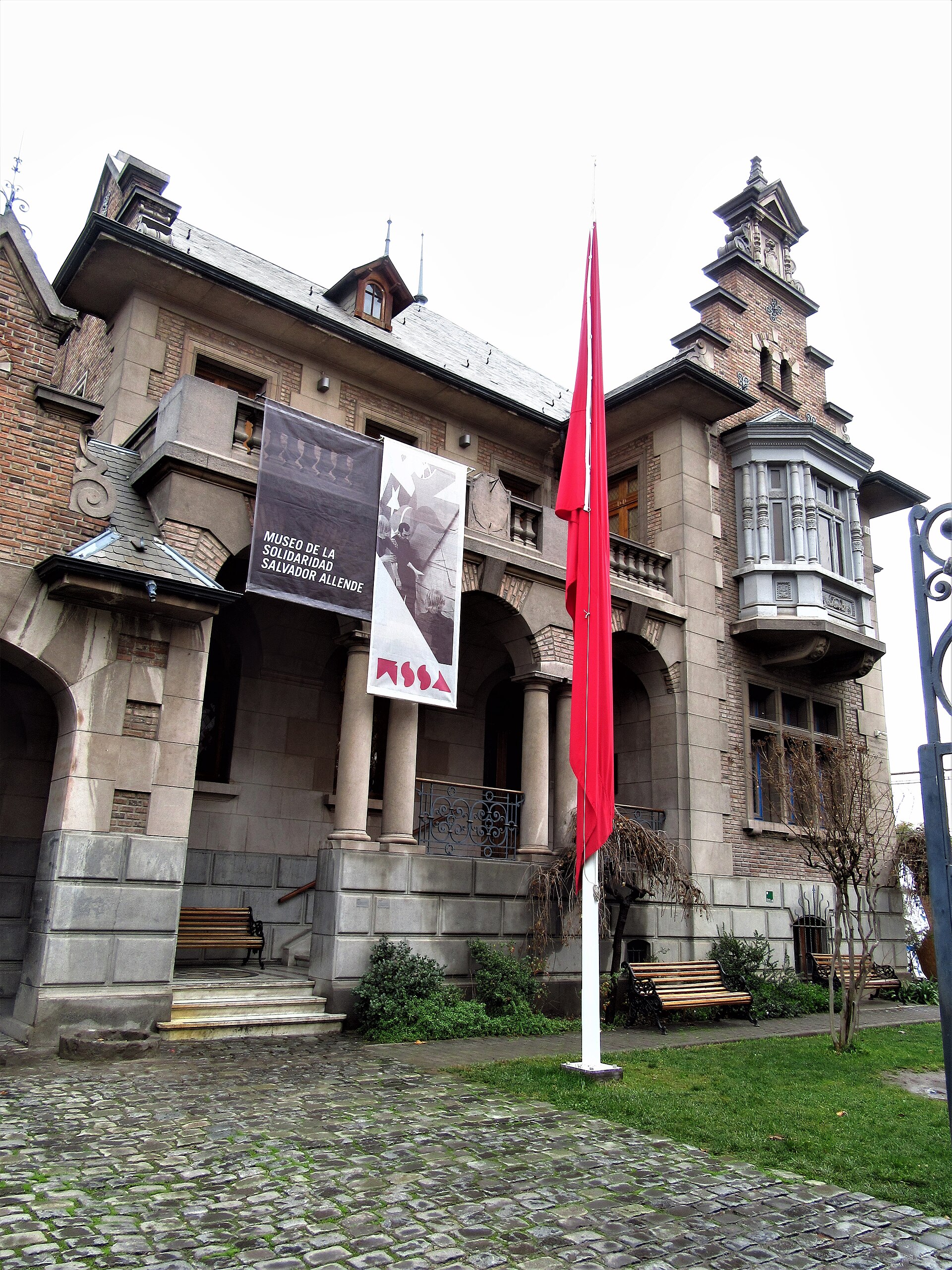 Ornate brick building housing the Museum of Solidarity Salvador Allende, with red banners, benches, and a cobblestone courtyard.