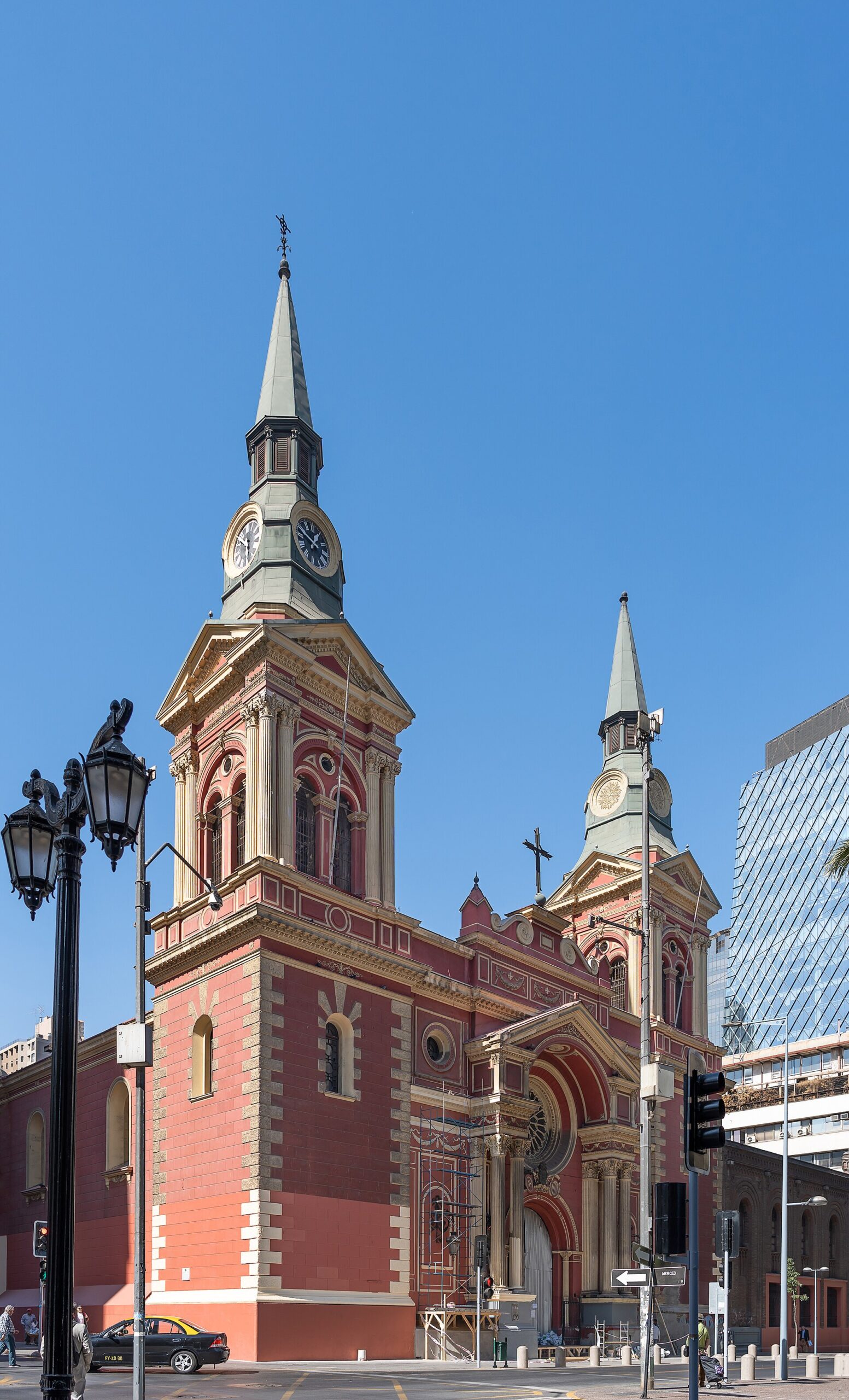 Ornate red Santiago church with clock towers and spires at a city intersection under a clear blue sky.