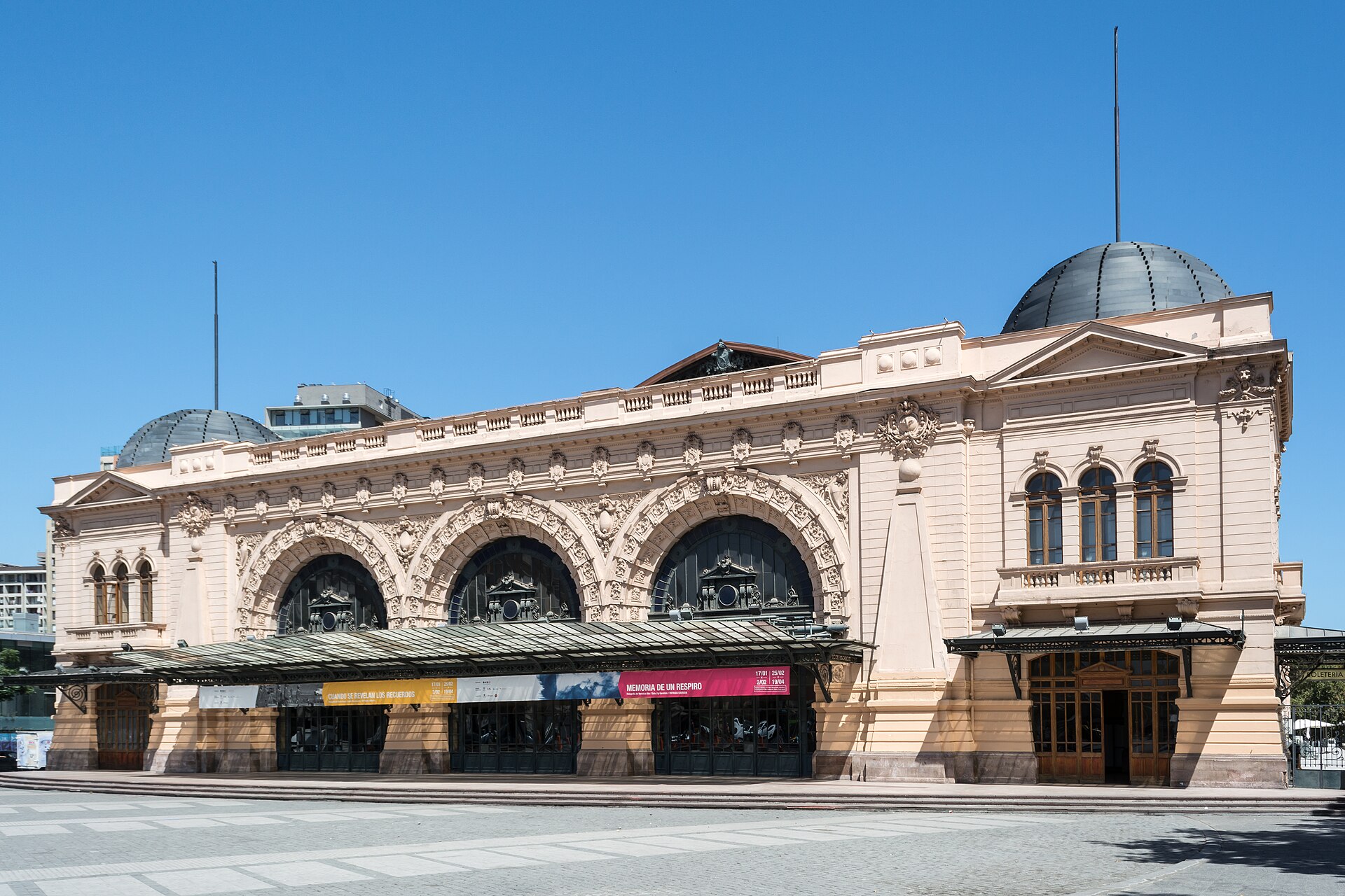 Ornate historic railway station with three arched entrances and domed roofs beneath a clear blue sky.
