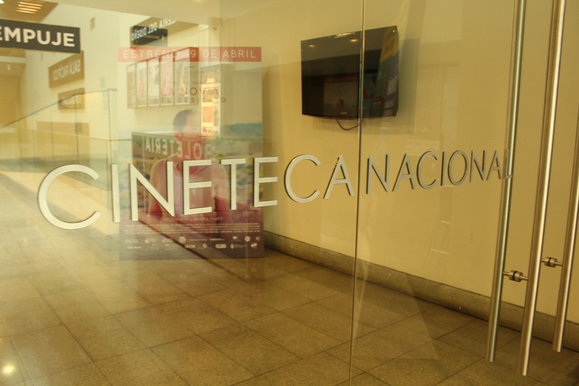 Glass entrance to Cineteca Nacional with large lettering, film posters, and a wall-mounted screen visible inside.