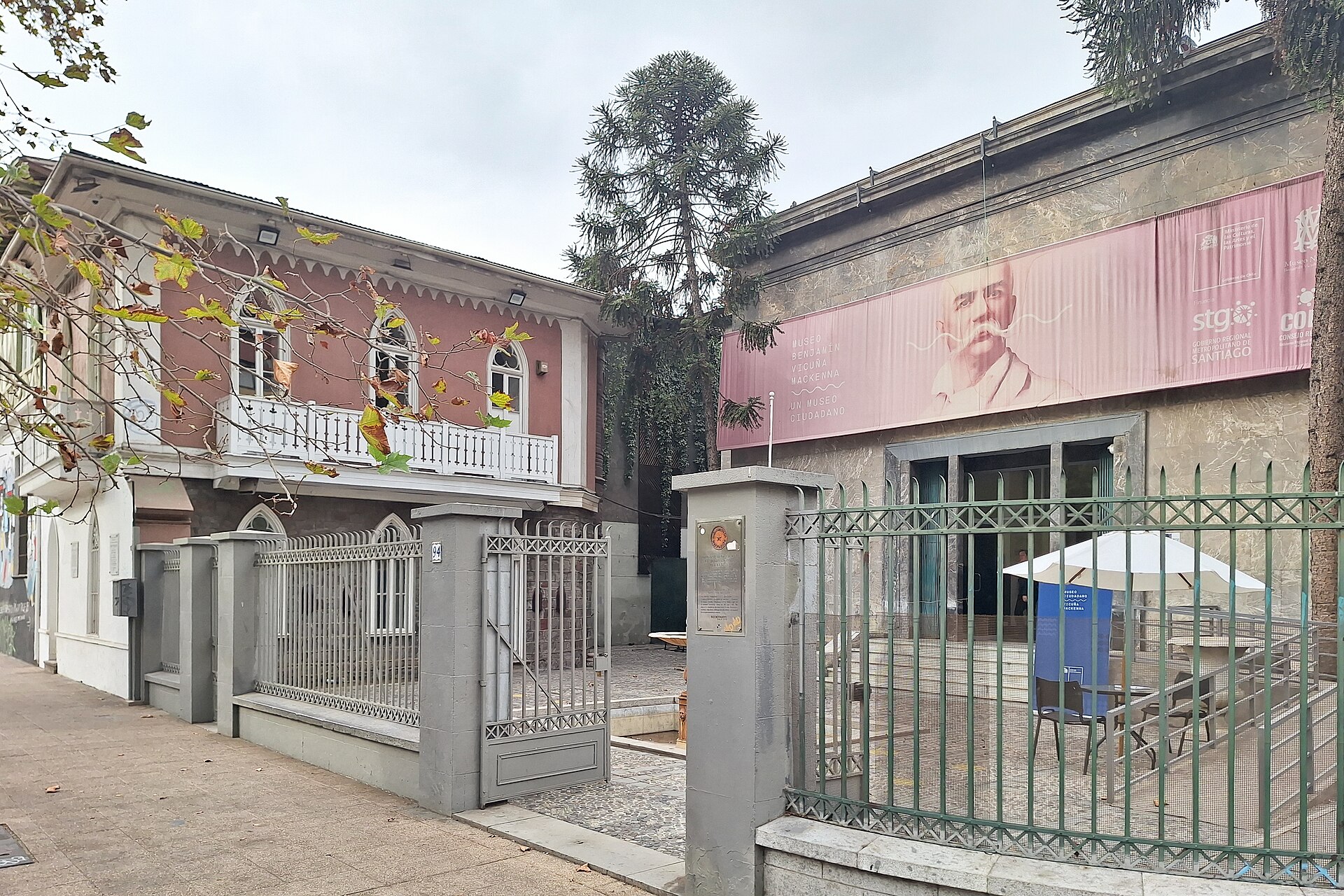 Street view of Museo Benjamín Vicuña Mackenna in Santiago, with a historic pink building beside the museum entrance and iron gates.