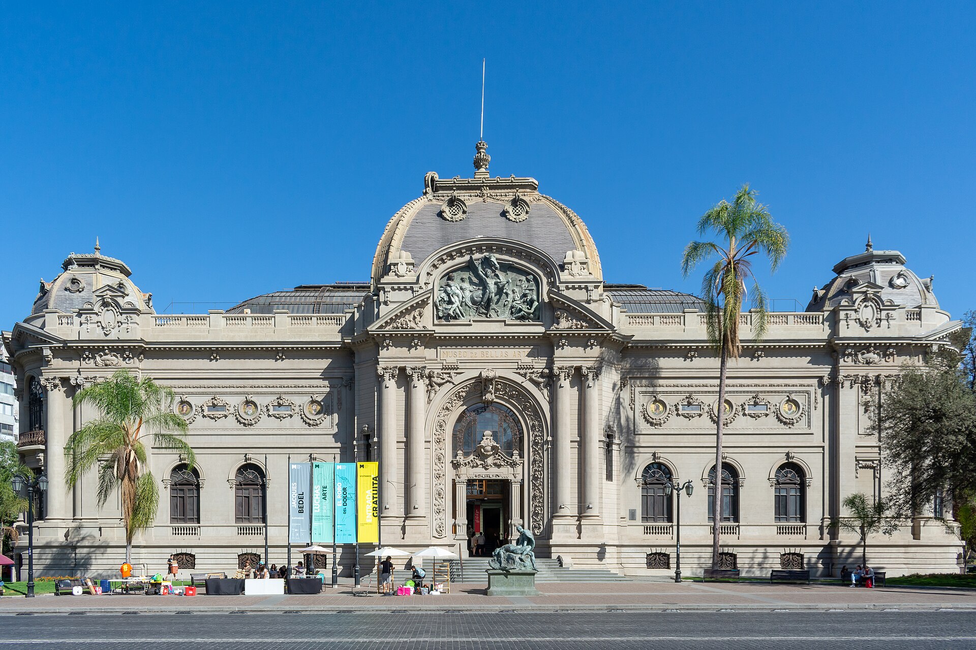 Ornate neoclassical Museo de Bellas Artes in Santiago, Chile, with a domed facade, palm trees, and a plaza statue under a clear blue sky.
