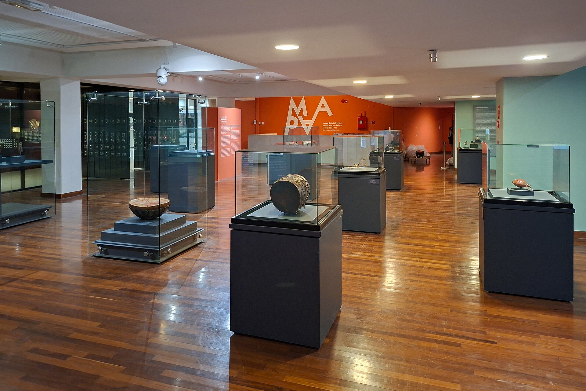 Interior of a folk art museum with drums and small artifacts displayed in glass cases on dark pedestals.