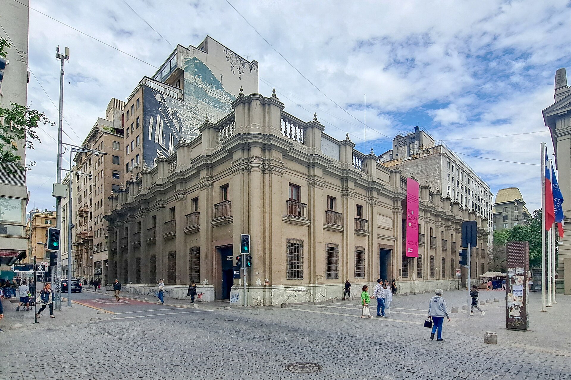 Historic neoclassical corner building on a busy cobblestone plaza in downtown Santiago, Chile, with pedestrians and surrounding high-rises.