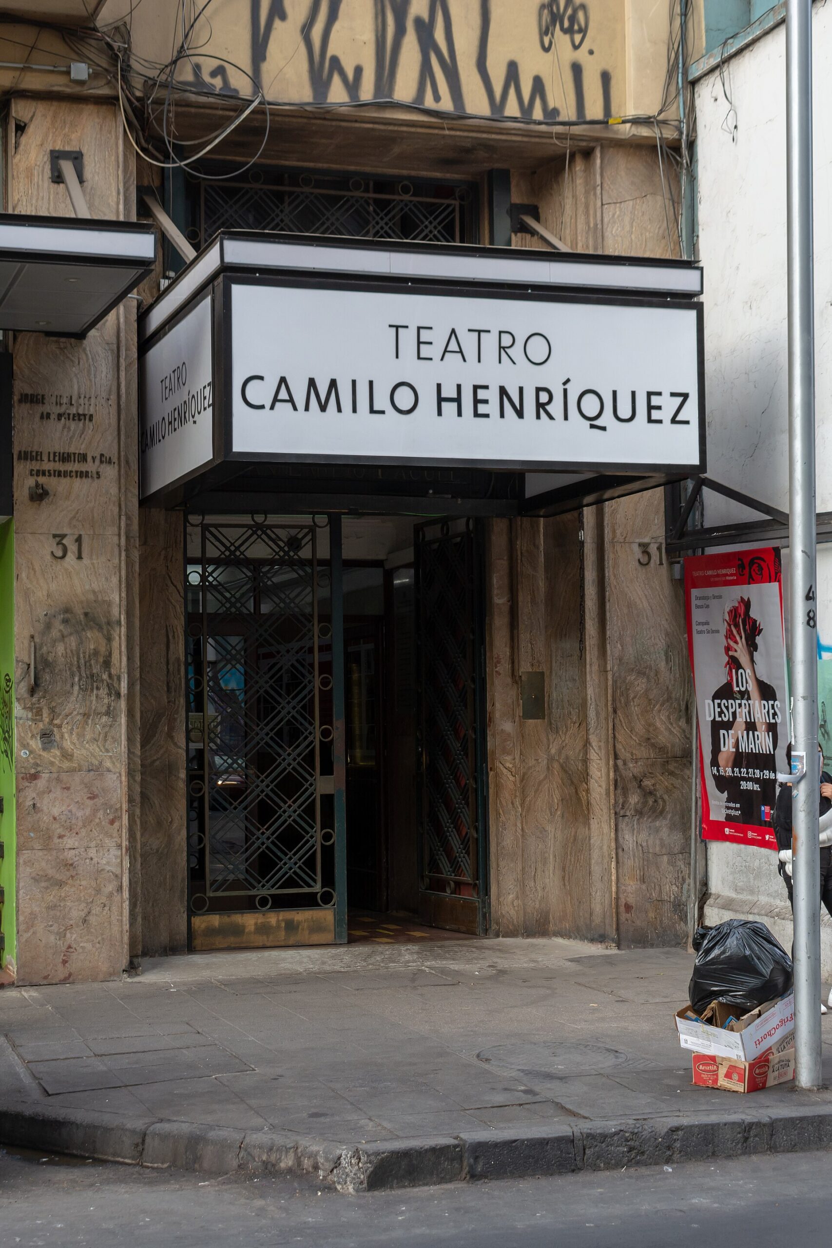 Entrance to Teatro Camilo Henríquez, with a stone facade, metal gates, theater sign, and a red play poster.
