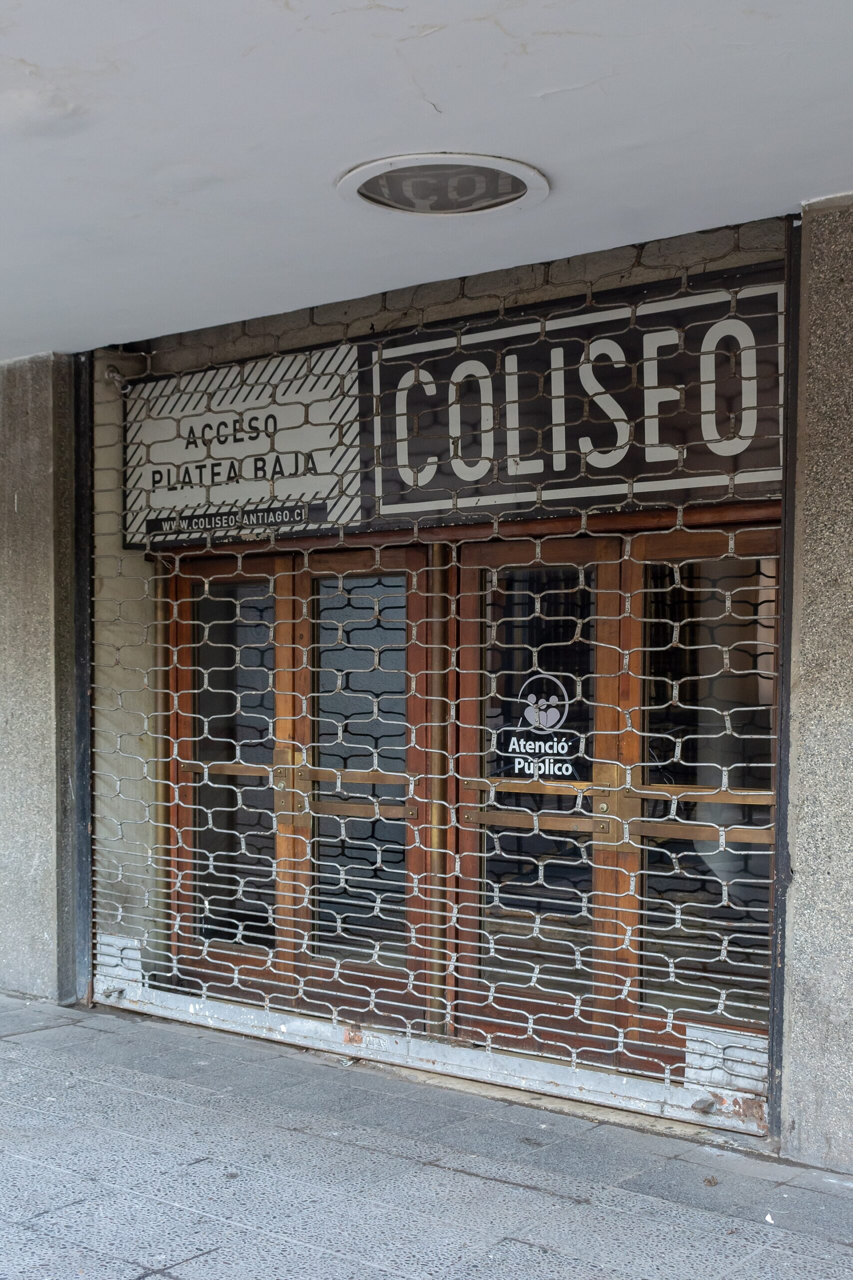 Closed metal security gate at Coliseo Santiago, with signs for public service and wheelchair-accessible lower-level seating.