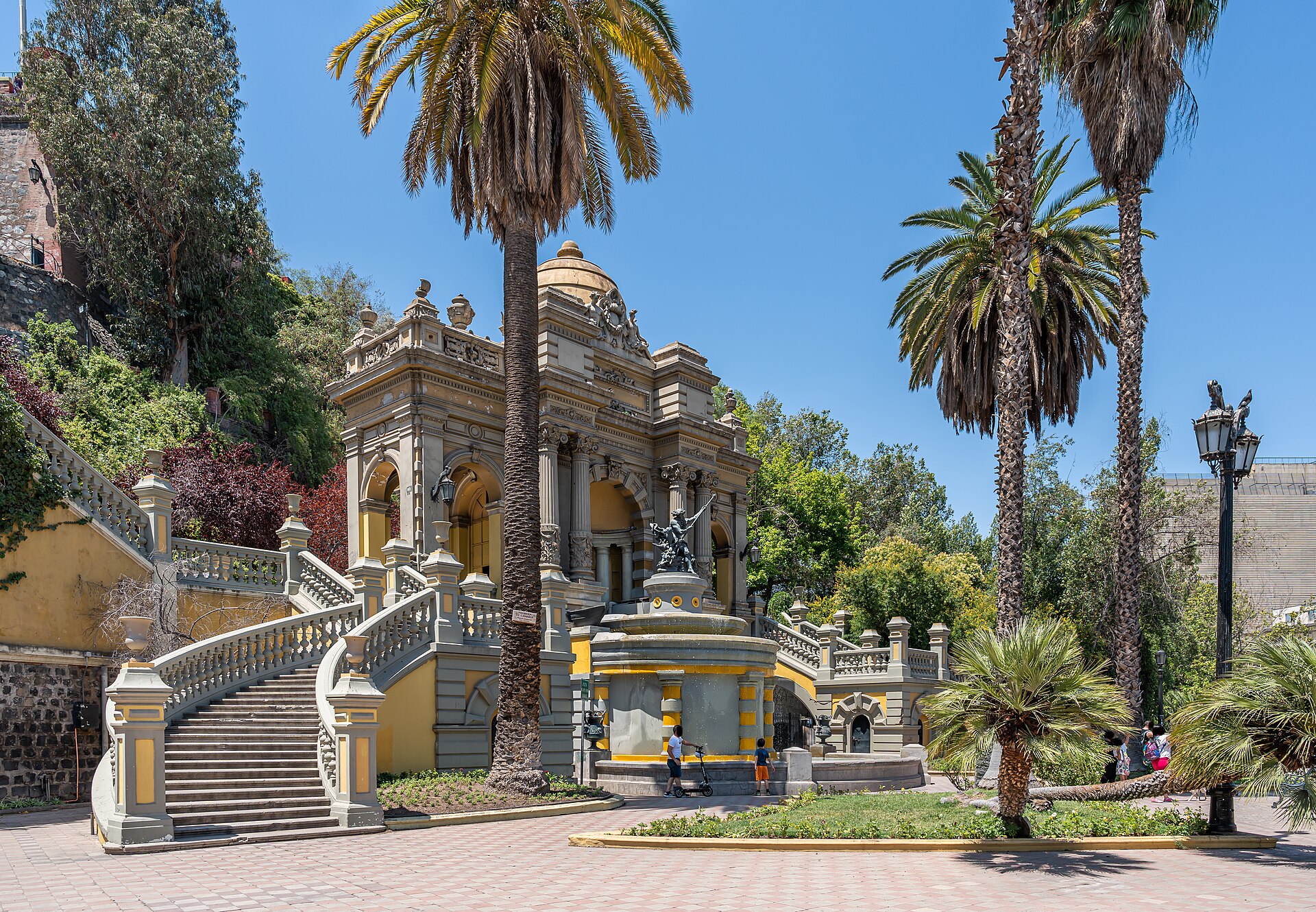 Ornate neoclassical fountain and staircase surrounded by palm trees in a sunny city plaza in Santiago, Chile.