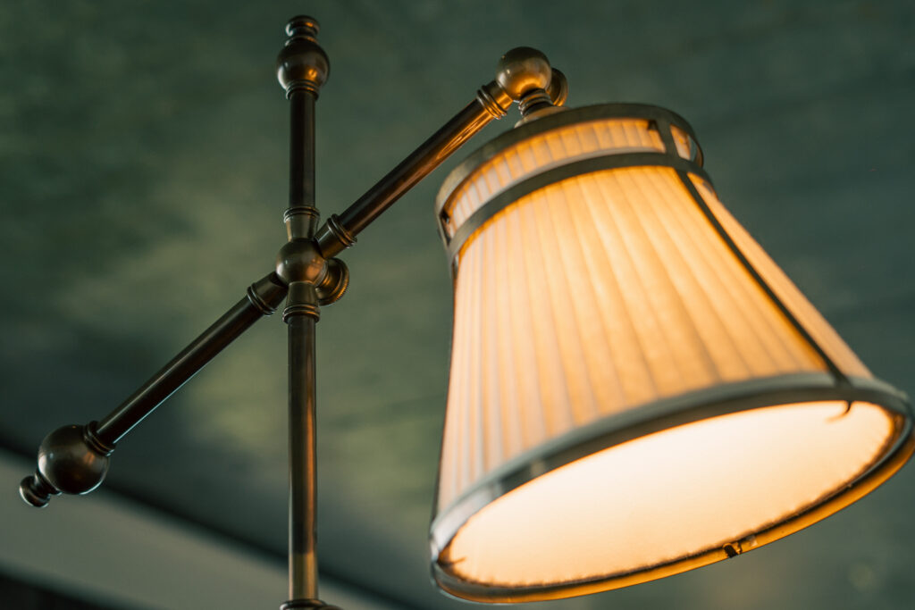 Primer plano de una lámpara de pie brillante con sombra de ámbar con un marco ajustable de metal oscuro adornado contra una pared verde.