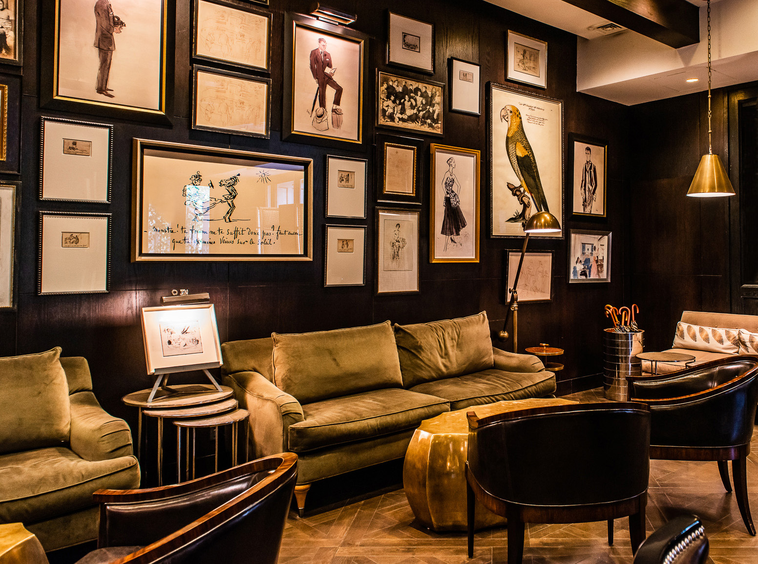 Elegant lounge with olive velvet sofas, dark leather chairs, brass lamps, and a gallery wall of framed artwork.