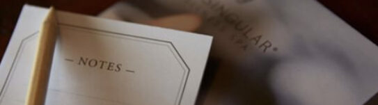 Screenshot Open notes notebook and pencil beside a blurred book on a wooden surface