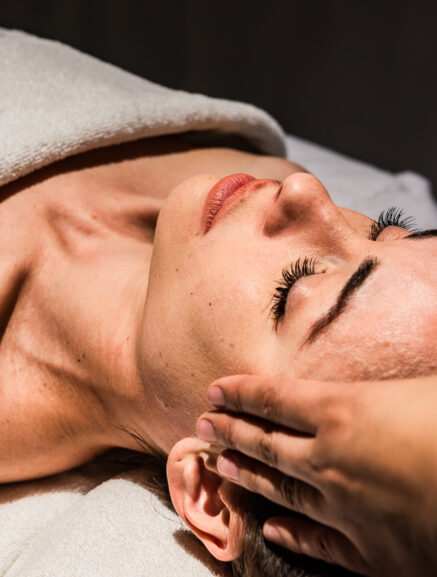 Woman receiving a relaxing facial massage at a spa, with a therapist gently massaging her face.