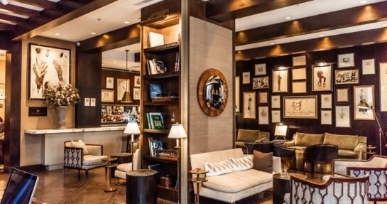 Elegant hotel lounge with plush seating, a stocked bar, dark wood beams, and a gallery wall of framed artwork.