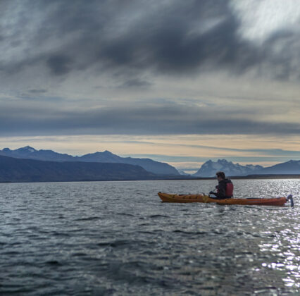 A kayaker paddles across a mountain lake beneath a dramatic cloudy sky.