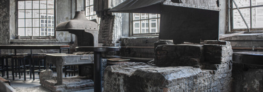 Abandoned industrial workshop with old brick furnaces, metal hoods, worktables, and large factory windows