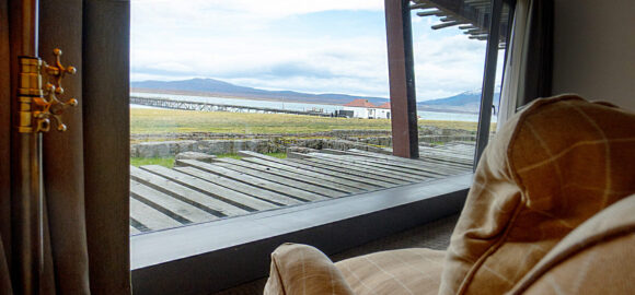 Cozy living room with a sofa and floor lamp overlooking a coastal landscape through a floor-to-ceiling window.