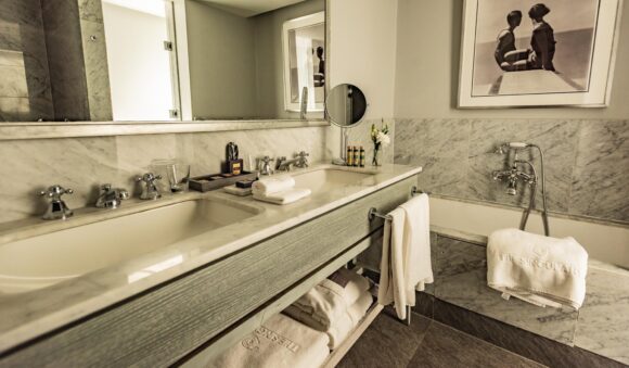 Luxury marble bathroom with double sinks, large mirror, bathtub, neatly folded towels, toiletries, flowers, and framed art.