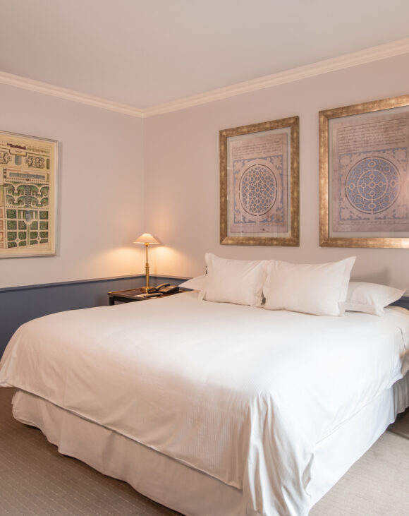 Elegant hotel bedroom with a white king bed, framed architectural prints, navy wall paneling, and warm bedside lamps.