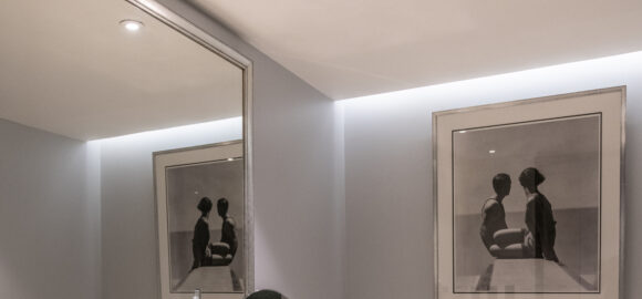 Elegant marble bathroom with a double-sink vanity, bathtub, wall mirror, and framed black-and-white artwork.