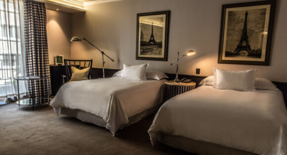 THE SINGULAR TWIN WITH BALCONY_DSC_6600-HDR-camas retocadas Elegant hotel room with two white beds, warm bedside lamps, patterned curtains, and framed Eiffel Tower prints.