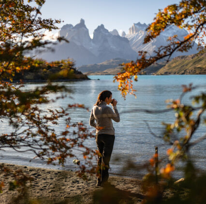 TORRES DEL PAINE - FULL DAY (66 de 1) Traveler photographing a turquoise lake and jagged mountains, framed by autumn foliage in Patagonia.