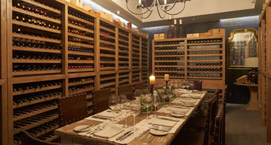 Comedor privado de bodega con botellero de madera, mesa, sillas de cuero y candelabro.