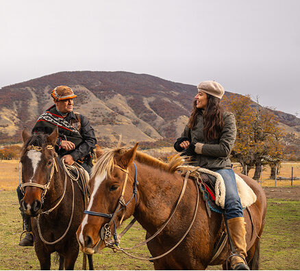 Two riders on horseback talk in a mountain pasture during autumn.